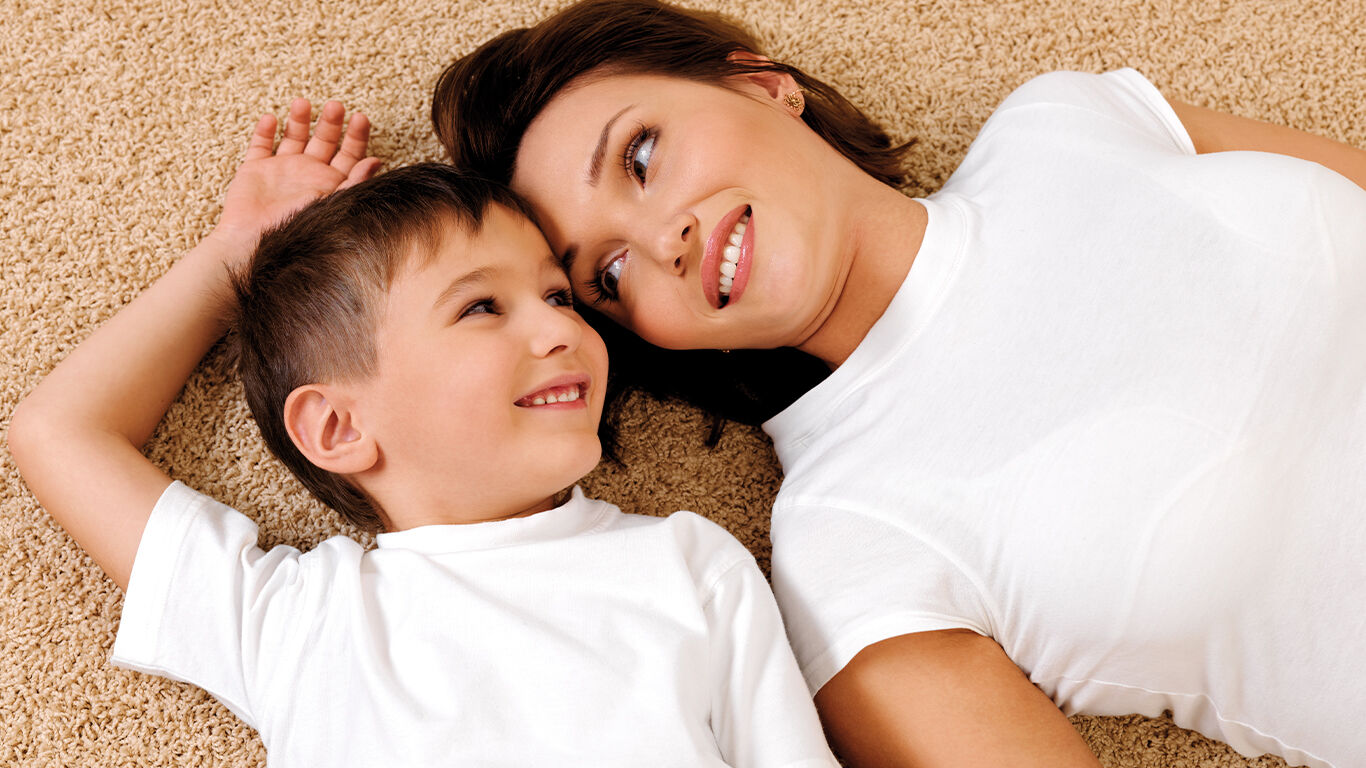 Mom and son laying on carpet looking at each other.
